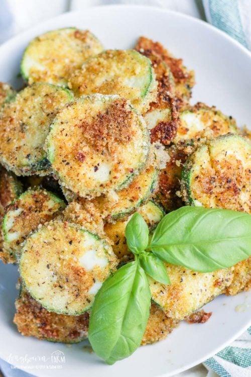 Fried parmesan zucchini on a plate garnished with basil. 