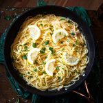 spaghetti with lemon sauce in a pan garnished with lemon slices and fresh herbs