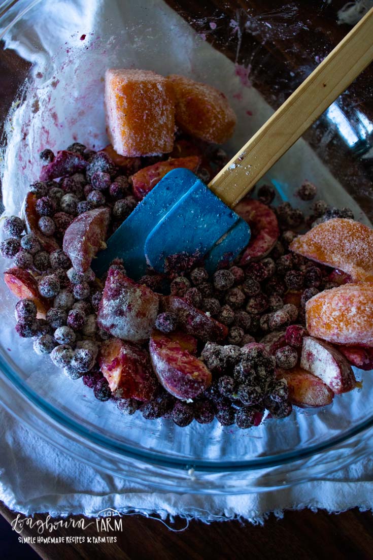 stirring frozen blueberries and peaches together in a bowl with a spatula