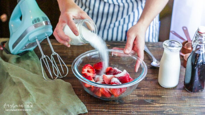 Adding sugar to the strawberries for easy homemade strawberry shortcake. 