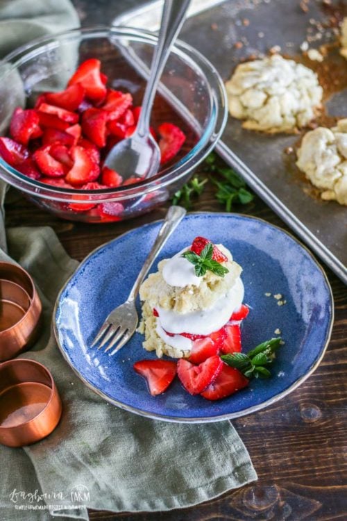Sheet tray with homemade shortcakes next to a bowl of strawberries and a made easy strawberry shortcake. 