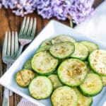 Zucchini cooked on the stovetop on a white square plate next to two small forks.