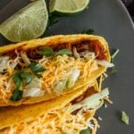 upclose view of cheese covered steak tacos with lime wedges to the side