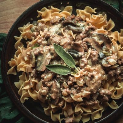 homemade beef stroganoff served over egg noodles on a plate, garnished with fresh herbs