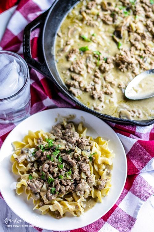 Vertical image of Plate of egg noodles next to the skillet of homemade easy beef stroganoff.