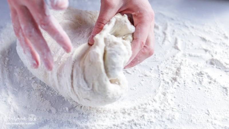 Folding dough back on itself for kneading homemade cinnamon rolls.