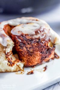 Baked and iced homemade cinnamon roll on a white plate.