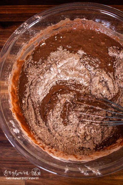 whisking together a chocolate batter in a glass bowl