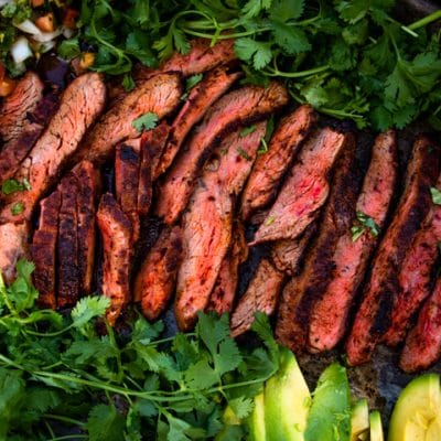 a close up of grilled flank steak next to avocados and herbs