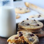 Broken homemade chocolate chip cookie in front of a glass of milk and more chocolate chip cookies.