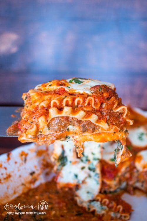 a side view of a slice of lasagna being held over a baking dish