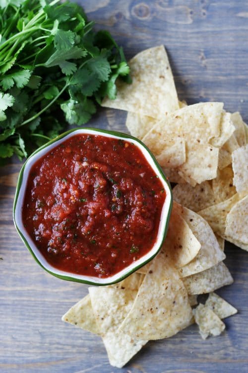Top view of restaurant style salsa next to some chips and cilantro.