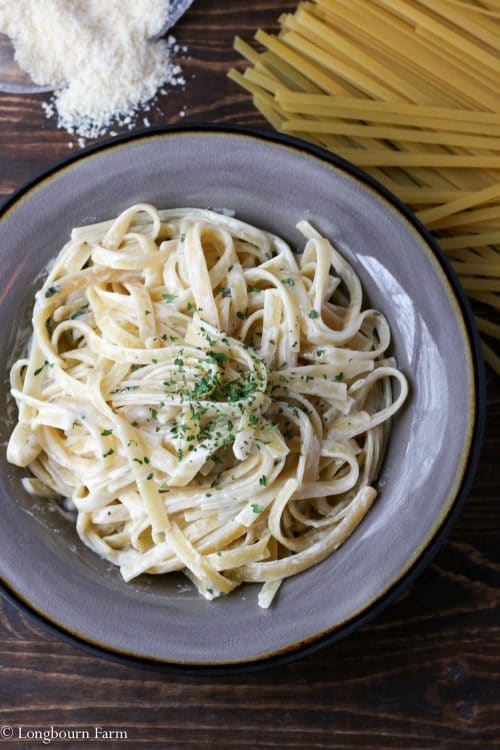 Quick alfredo pasta recipe in a bowl with dry noodles and parmesan in the background.