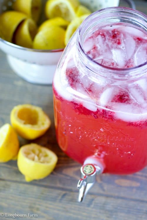 Vat of raspberry lemonade next to spent lemon halves.