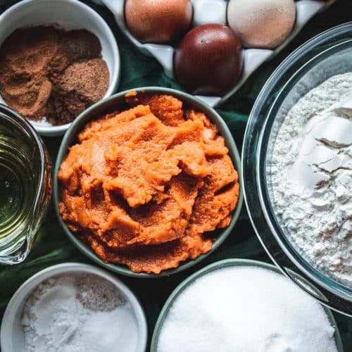 ingredients for layered pumpkin cake, eggs, pumpkin puree, flour, sugar and spices all in bowls.