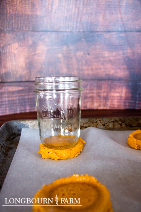 glass jar pressing down the pumpkin cookie dough balls on baking sheet