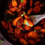 a close up of glazed carrots with a wooden spoon scooping some out