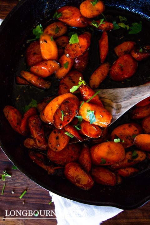 a close up of glazed carrots with a wooden spoon scooping some out