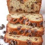 Three slices of chocolate chip banana bread lying down in front of the loaf of chocolate chip banana bread.