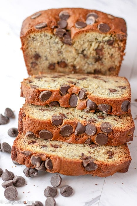 Three slices of chocolate chip banana bread lying down in front of the loaf of chocolate chip banana bread.