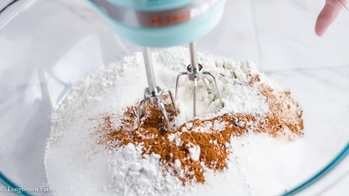 A ice blue kitchen aid hand mixer just beginning to mix the dry ingredients for cinnamon muffins.
