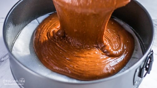 Pouring basic chocolate cake recipe batter into a springform pan lined with parchment paper.
