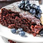 Closeup, side view, of a slice of basic chocolate cake topped with blueberries.
