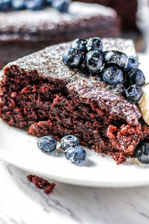 Closeup, side view, of a slice of basic chocolate cake topped with blueberries. 