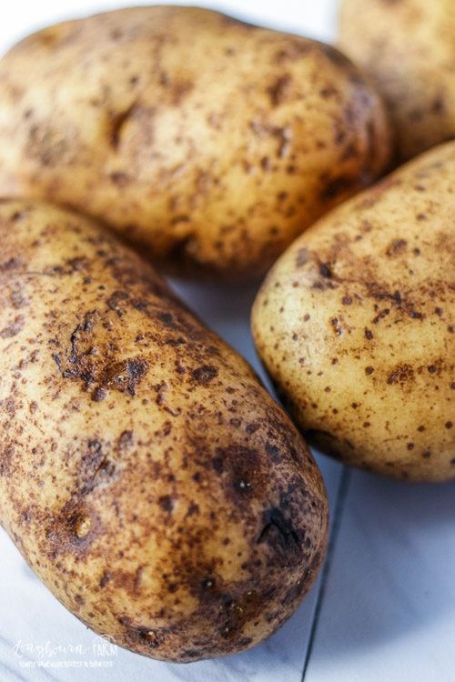 A group of 4 russet potatoes on a white board.