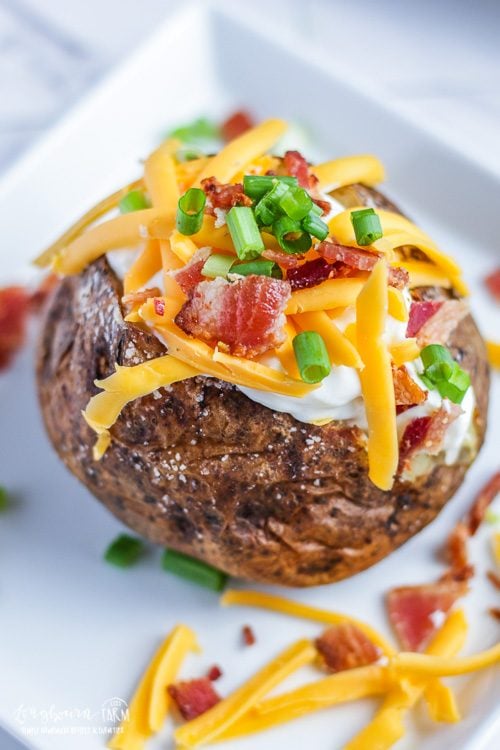 Side, front view of a baked potato loaded with sour cream, cheese, bacon, and green onions.