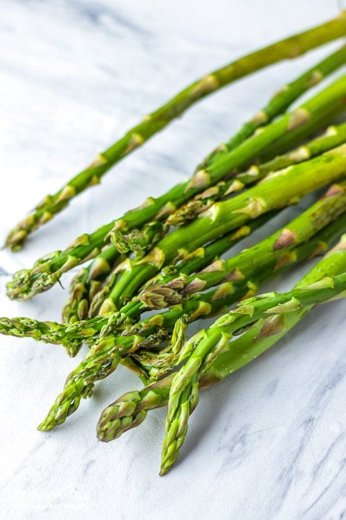 Pile of asparagus spears on a tile marble counter.