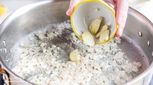 Adding garlic cloves to the sautéed shallow for lemon cream sauce.