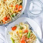 Pasta primavera recipe on a white plate next to a glass of water and the pan of pasta primavera.