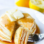 Forkful of lemon ricotta pancakes resting on a plate with lemon ricotta pancakes.