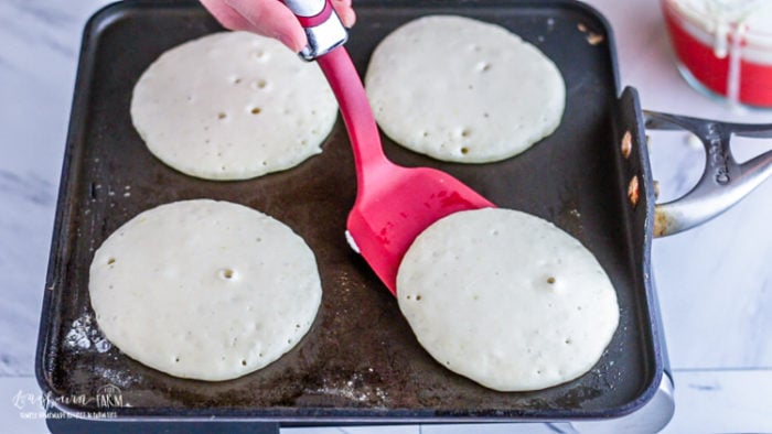 Flipping lemon ricotta pancakes over with a red spatula.