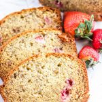 Three slices of strawberry banana bread next to some loose strawberries.
