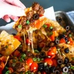 a hand pulling up a ground beef nacho chip with toppings and stringy melted cheese