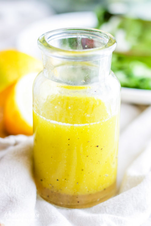 Lemon salad dressing in a glass jar with lemons in the background.