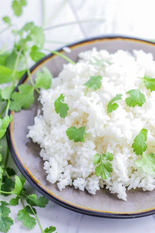 Top angled view of a plate of white rice with cilantro sprinkled on top. 