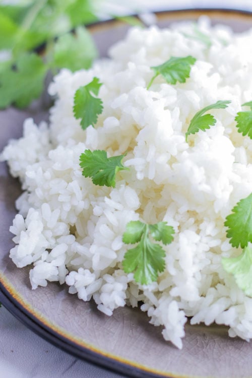 Side view of a plate of white rice with cilantro sprinkled on top.