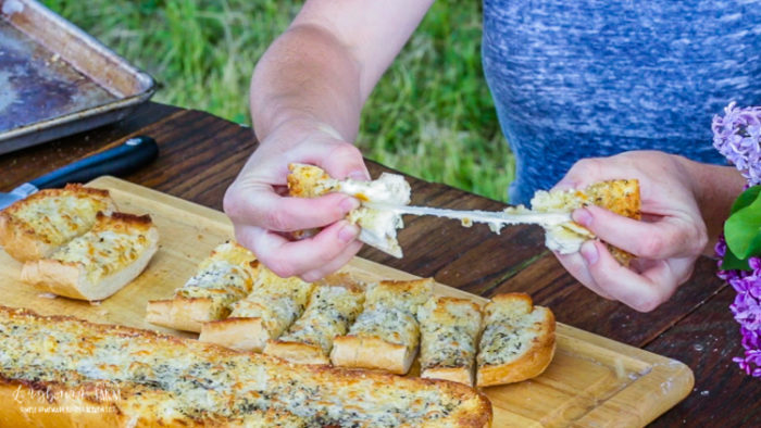 Breaking and pulling apart a slice of cheesy garlic bread.