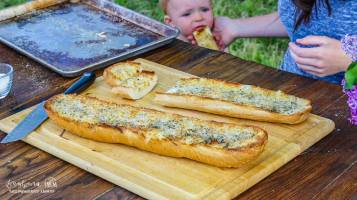Cute baby sneaking some cheesy garlic bread from the cutting board.