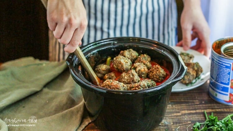 Adding meatballs to the sauce for meatball sandwiches.