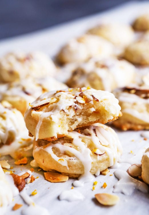 These Almond Cookies are melt-in-your-mouth delicious and super easy to make! The cookies have a chewy texture with crunchy bits of almond. They are topped with an almond glaze and a touch of orange zest that will leave you wanting more (and more and more)! #almondcookies #almondcookiesrecipe #almondcookierecipe #almondcookiesrecipeeasy #chocolatealmondcookies #christmascookies