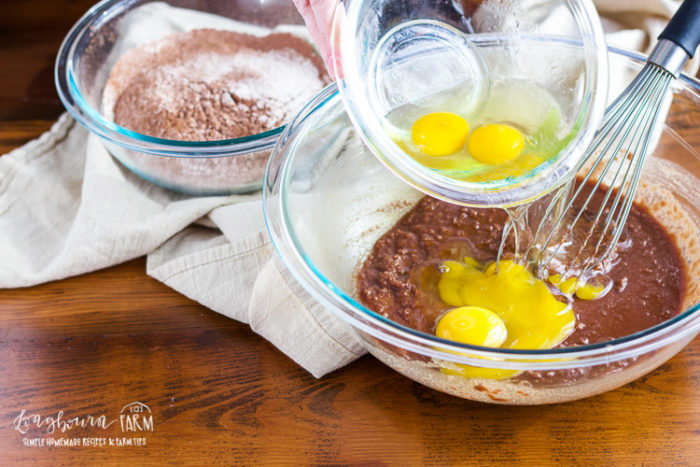 Adding eggs to the melted chocolate mixture for brownies from scratch. 