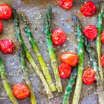 Oven roasted asparagus and tomatoes on a sheet pan sprinkled with parmesan cheese.