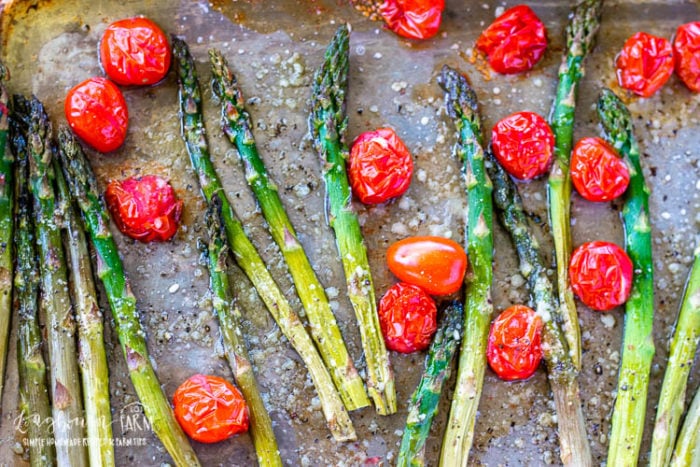 Oven roasted asparagus and tomatoes on a sheet pan sprinkled with parmesan cheese. 