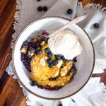 a bowl filled with dutch oven blueberry cobbler and vnailla ice cream