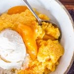a close up of a bowl of peach cobbler with vanilla ice cream and a spoon