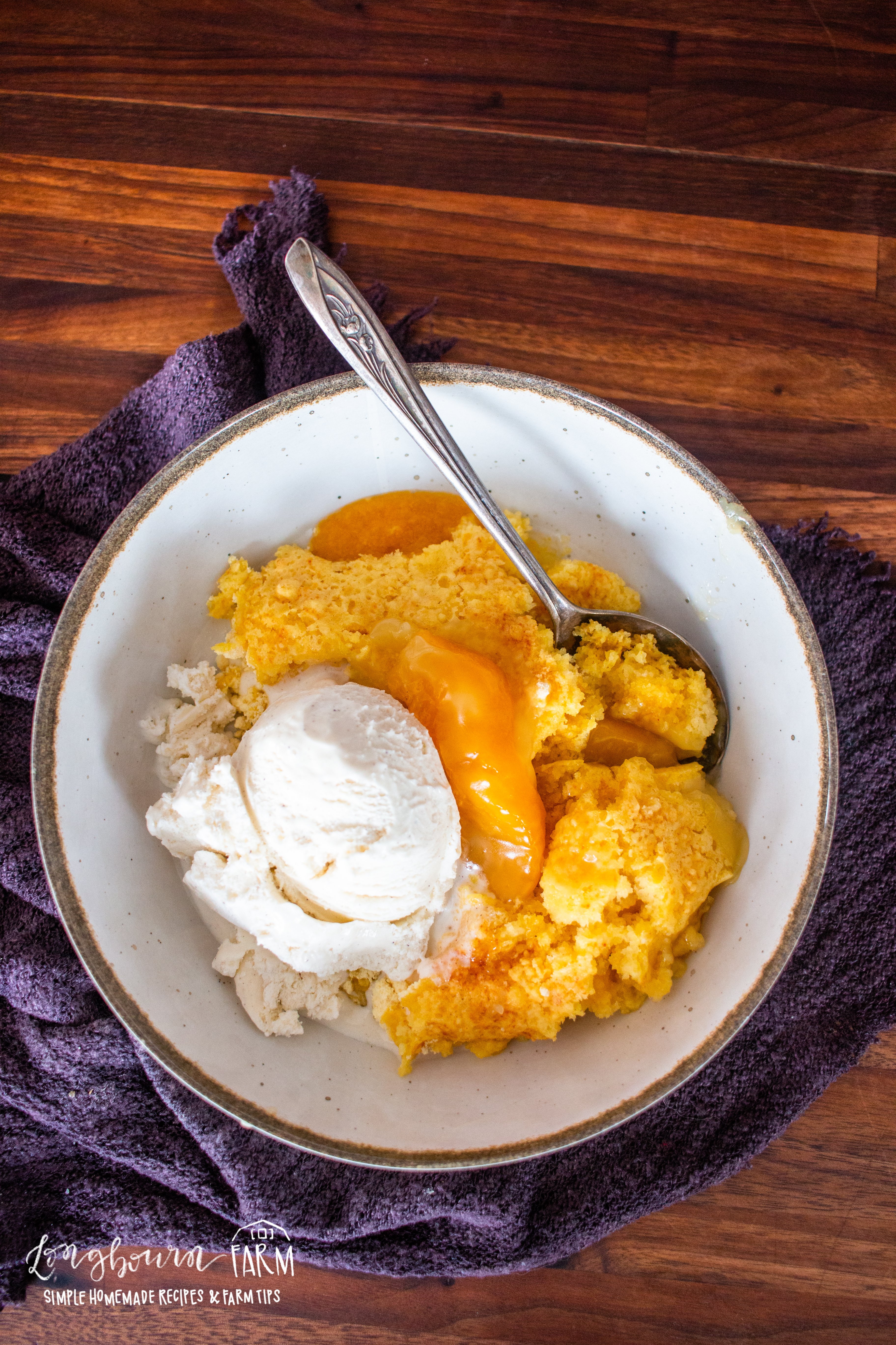 dutch oven peach cobbler in a bolw with ice cream and a spoon